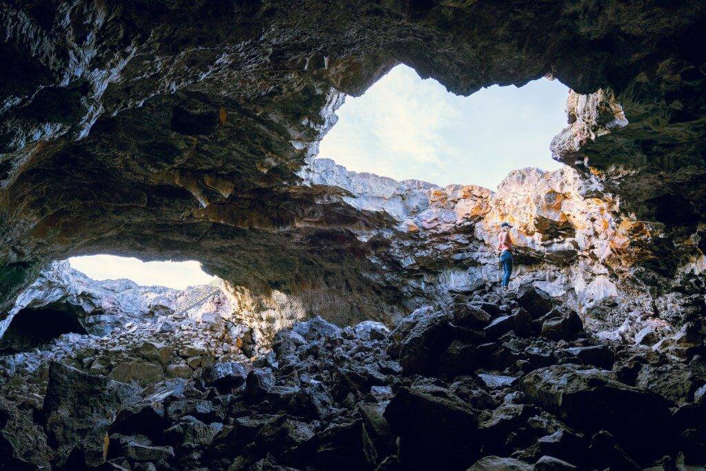 woman standing inside large rock tube/tunnel looking up at hole in top of tunnel