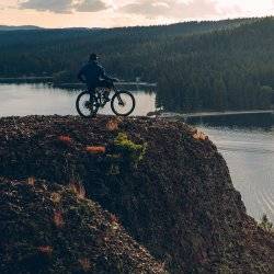 a person on a mountain bike on a hill overlooking a lake with tree covered mountains in the distance