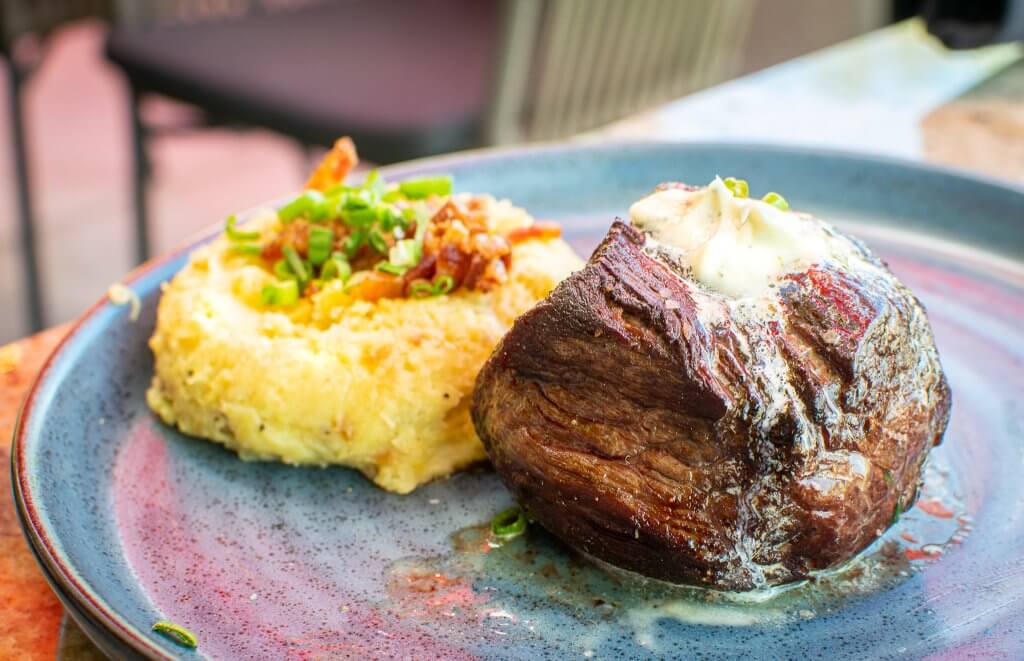 En el centro de un plato azulado se encuentra un filete con una porción de puré de papas con guarnición a un lado.