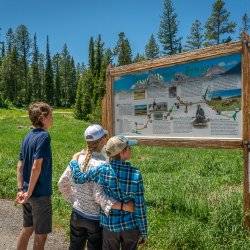 Three people standing in front of interpretive sign along the Teton Scenic Byway in Idaho.