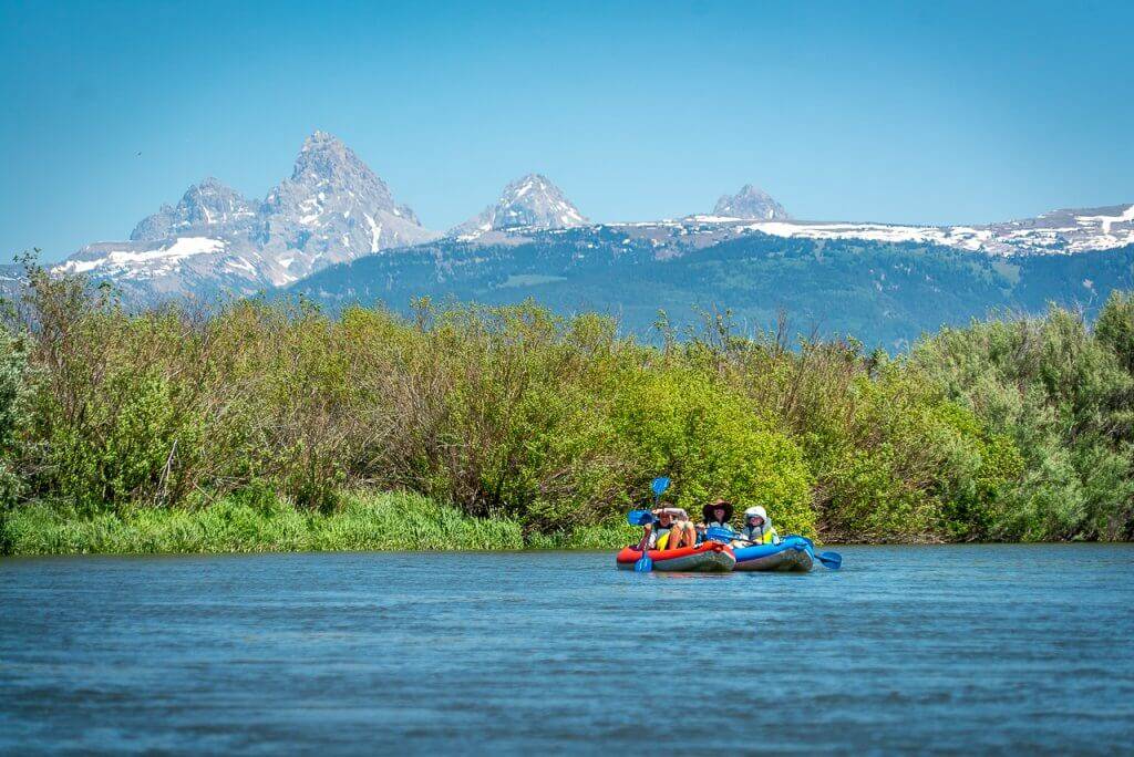 two people in inflatable kayaks with Teton mountains in background