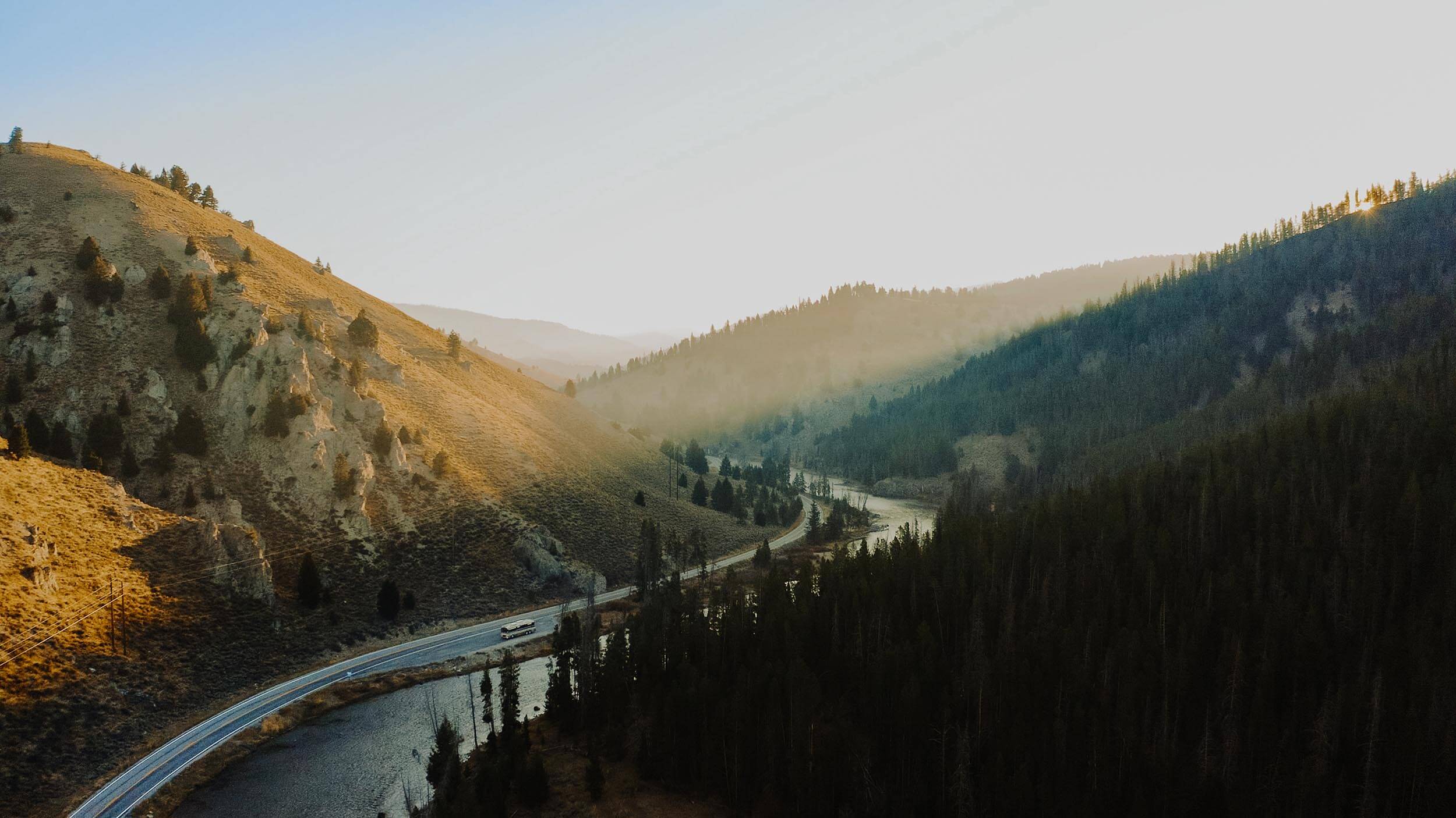 a winding road running alongside a river, surrounded by tree covered mountains