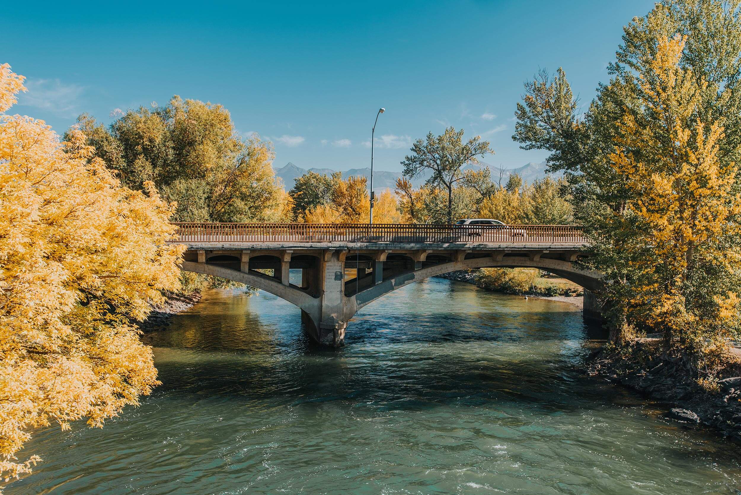 side view of a bridge over a river surrounded by yellow and green trees