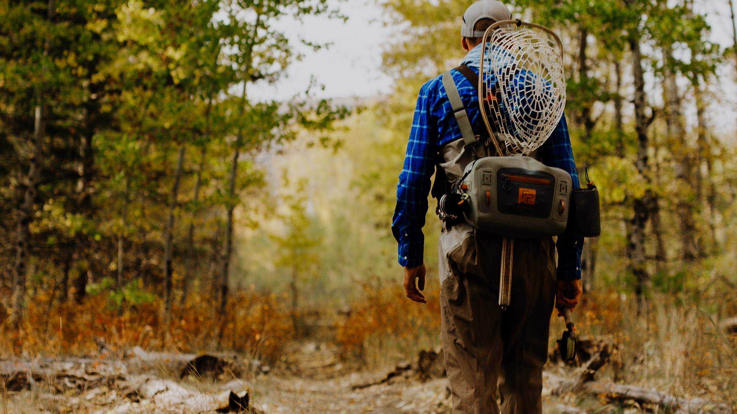 a person with fishing gear walking through a forest of trees