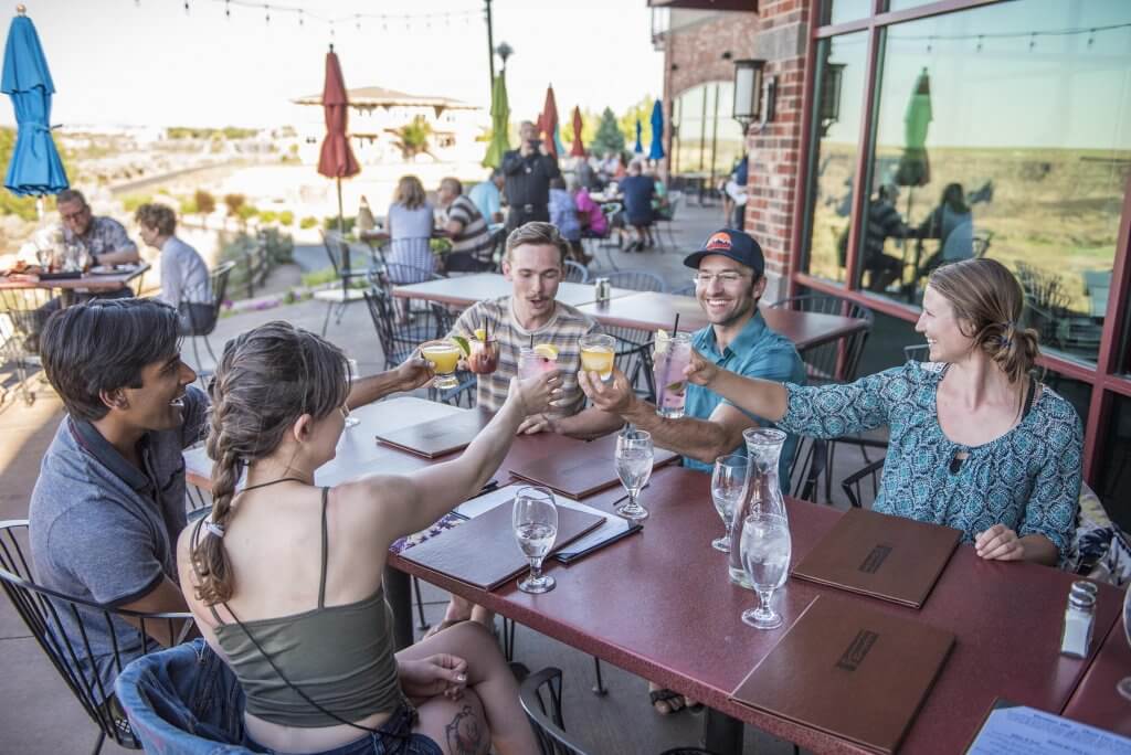 A group of five people seated at a table raising their glasses together in a cheers on a patio at Elevation 486.