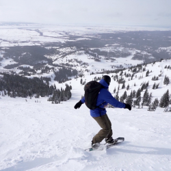 A snowboarder in a blue jacket at the top of a ski run at Grand Targhee Resort.