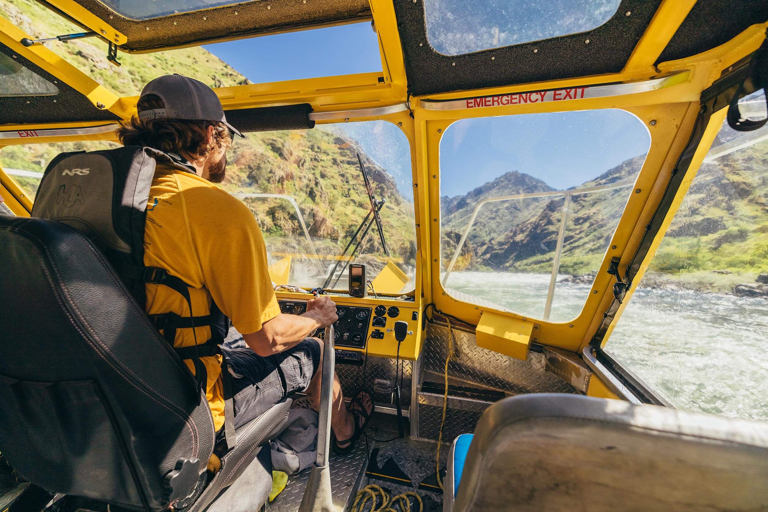 a man steering a jet boat on a river within a canyon