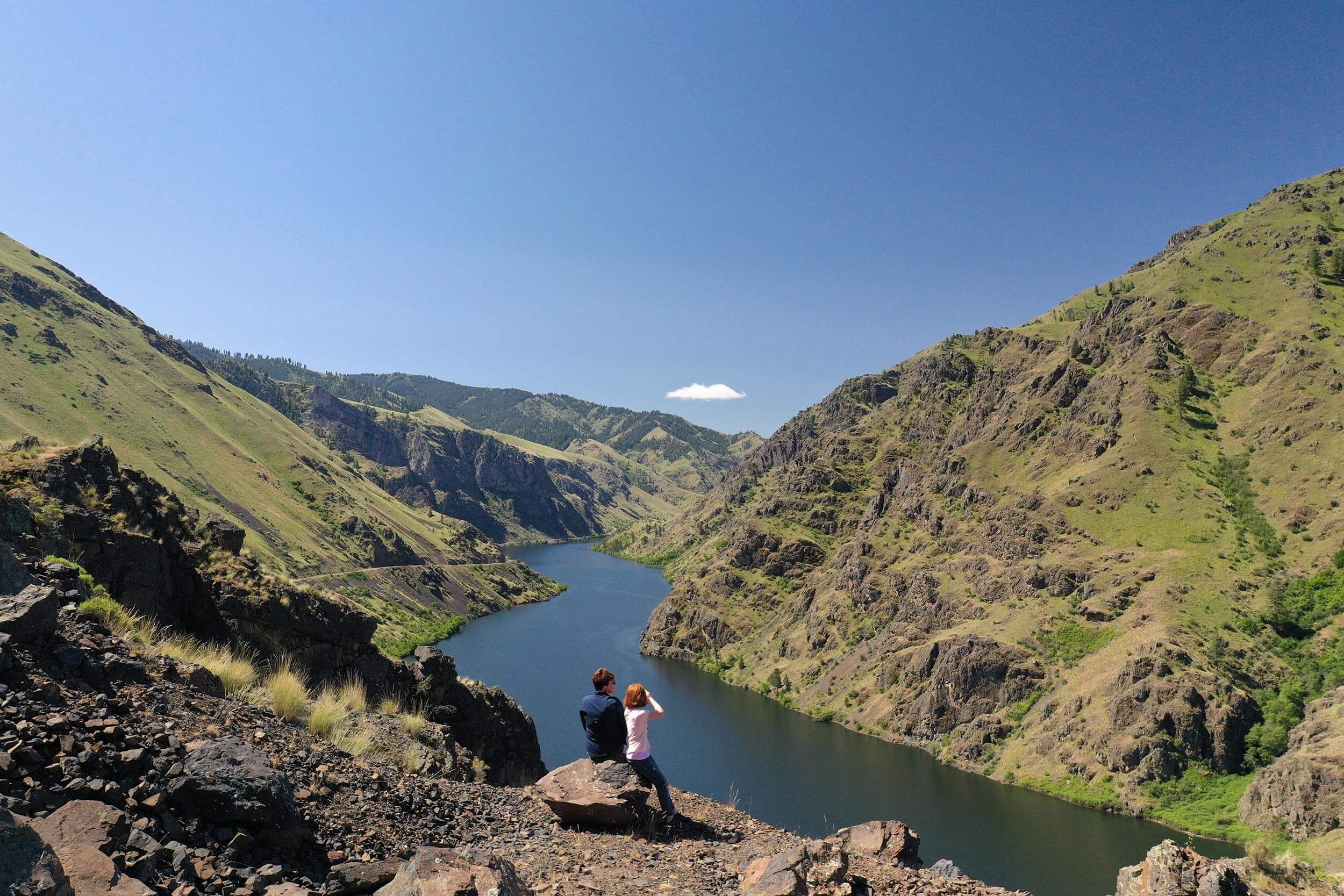 two people sitting on a rock looking out over a river running through Hells Canyon Idaho.