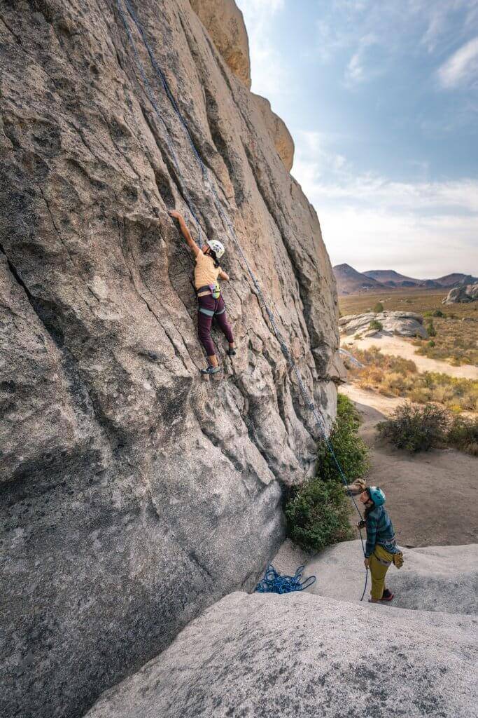 woman climbing rock face while partner holds rope below