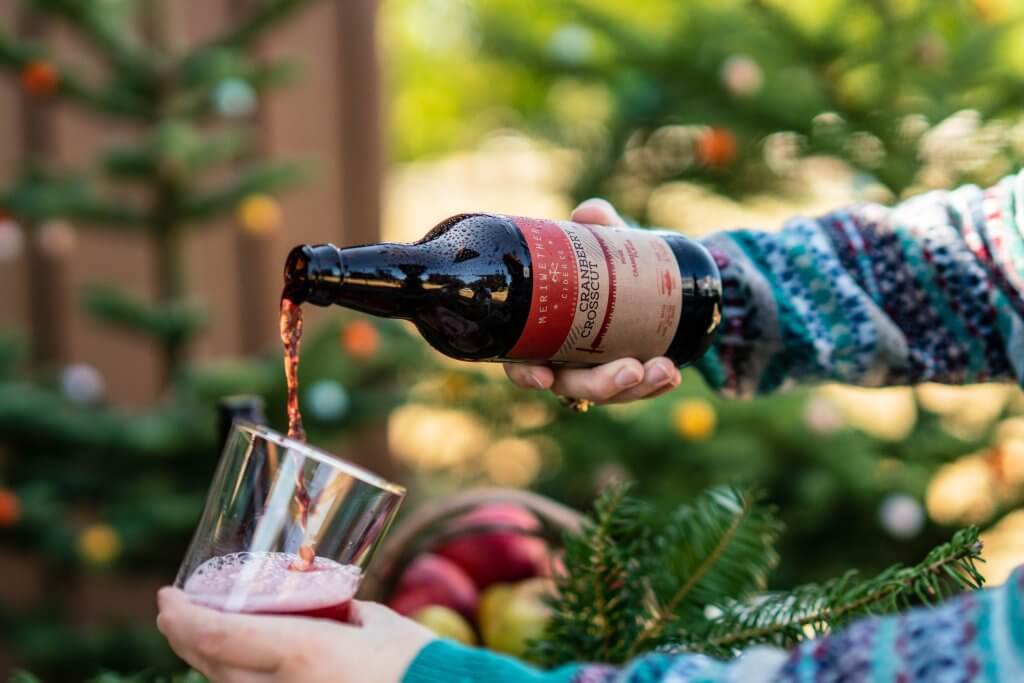 A person in a sweater pouring a glass of red cider from Meriwether Cider Company.