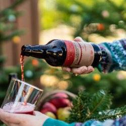 A person in a sweater pouring a glass of red cider from Meriwether Cider Company.