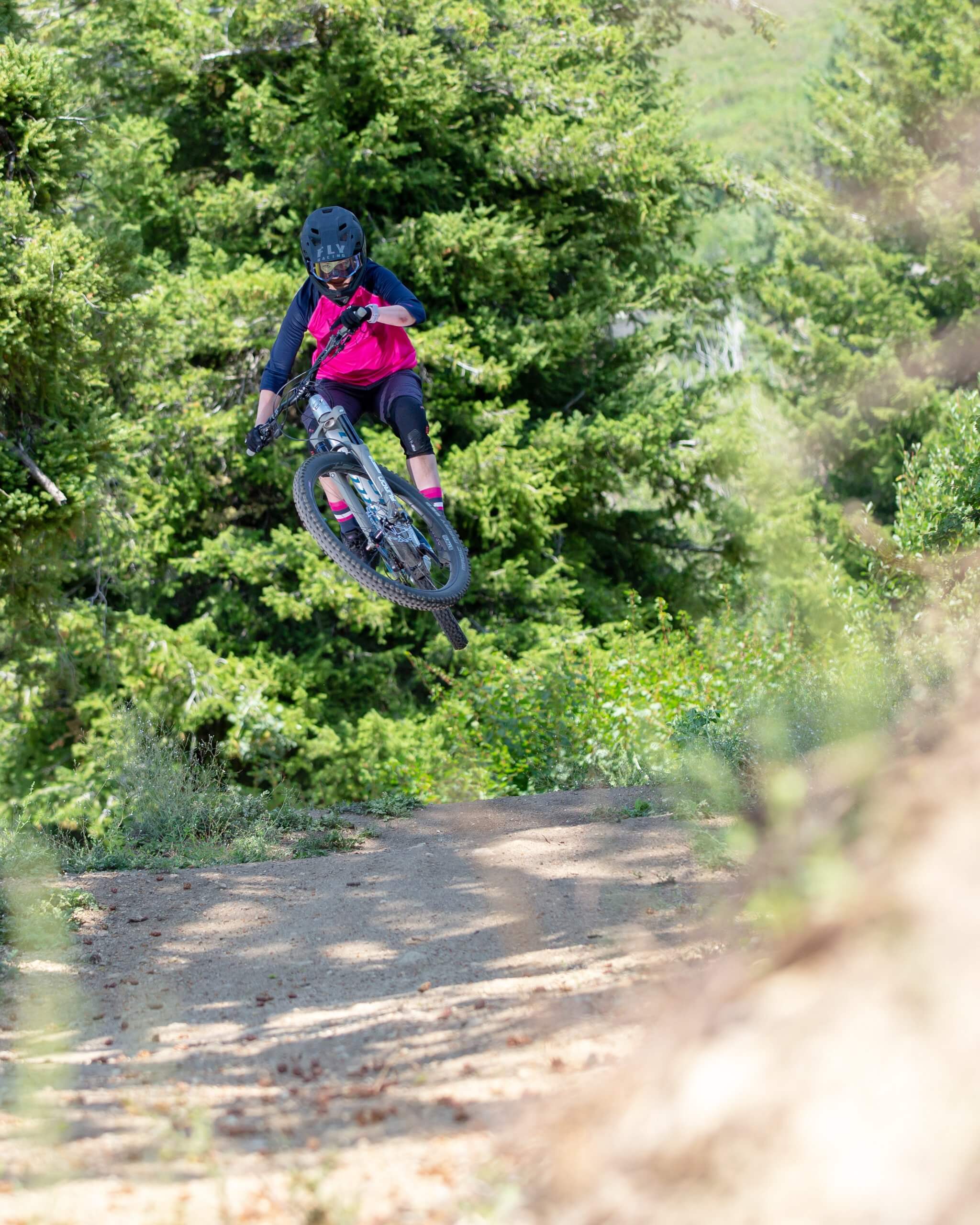 April Zastrow rides her mountain bike and makes a jump while dressed in pink and black