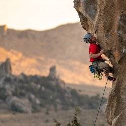 a person in red, wearing a helmet, climbs a cliff at the City of Rocks in Almo, Idaho