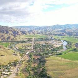 An overhead view of a river running through a sprawling green landscape with mountains in the background.