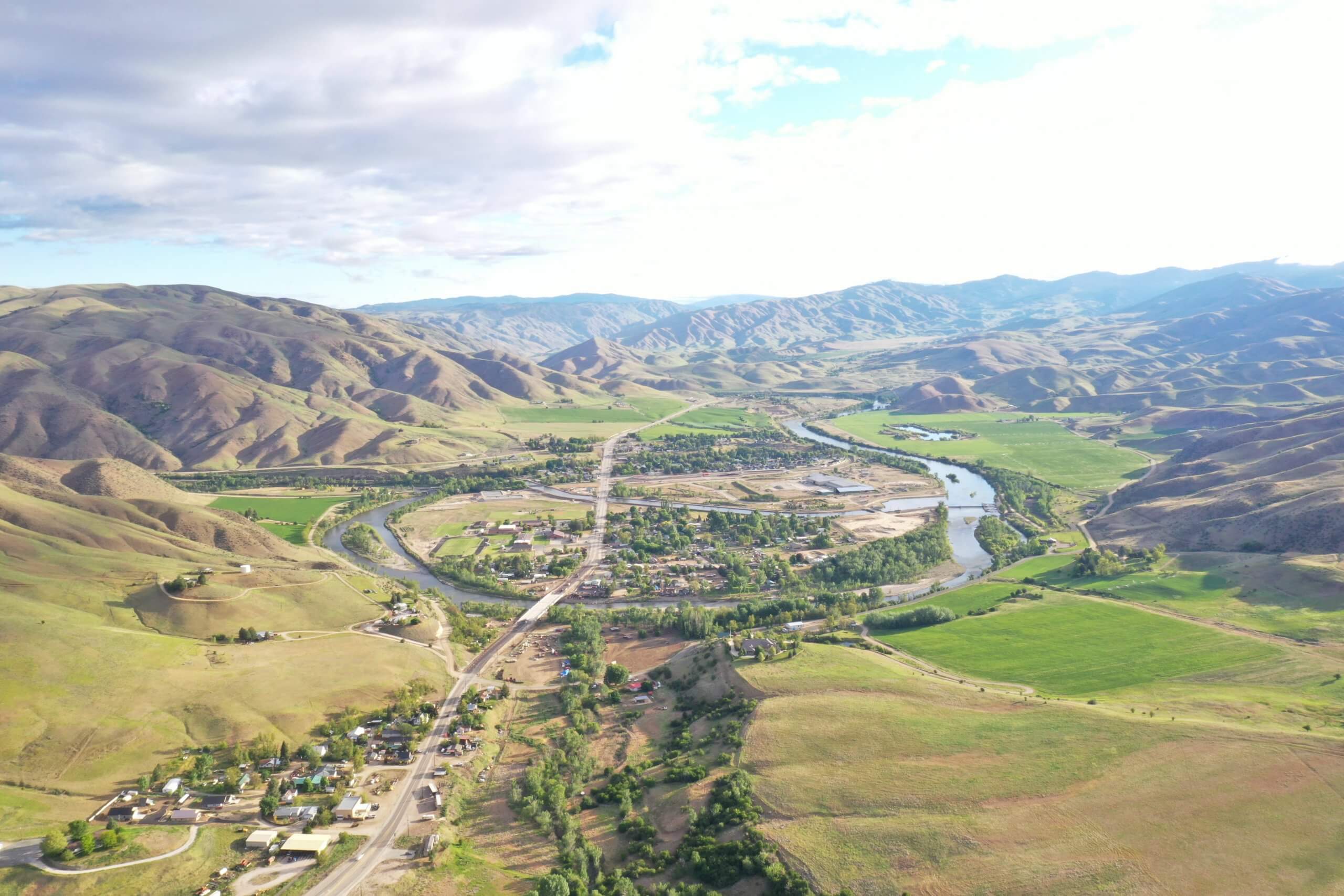 An overhead view of a river running through a sprawling green landscape with mountains in the background.