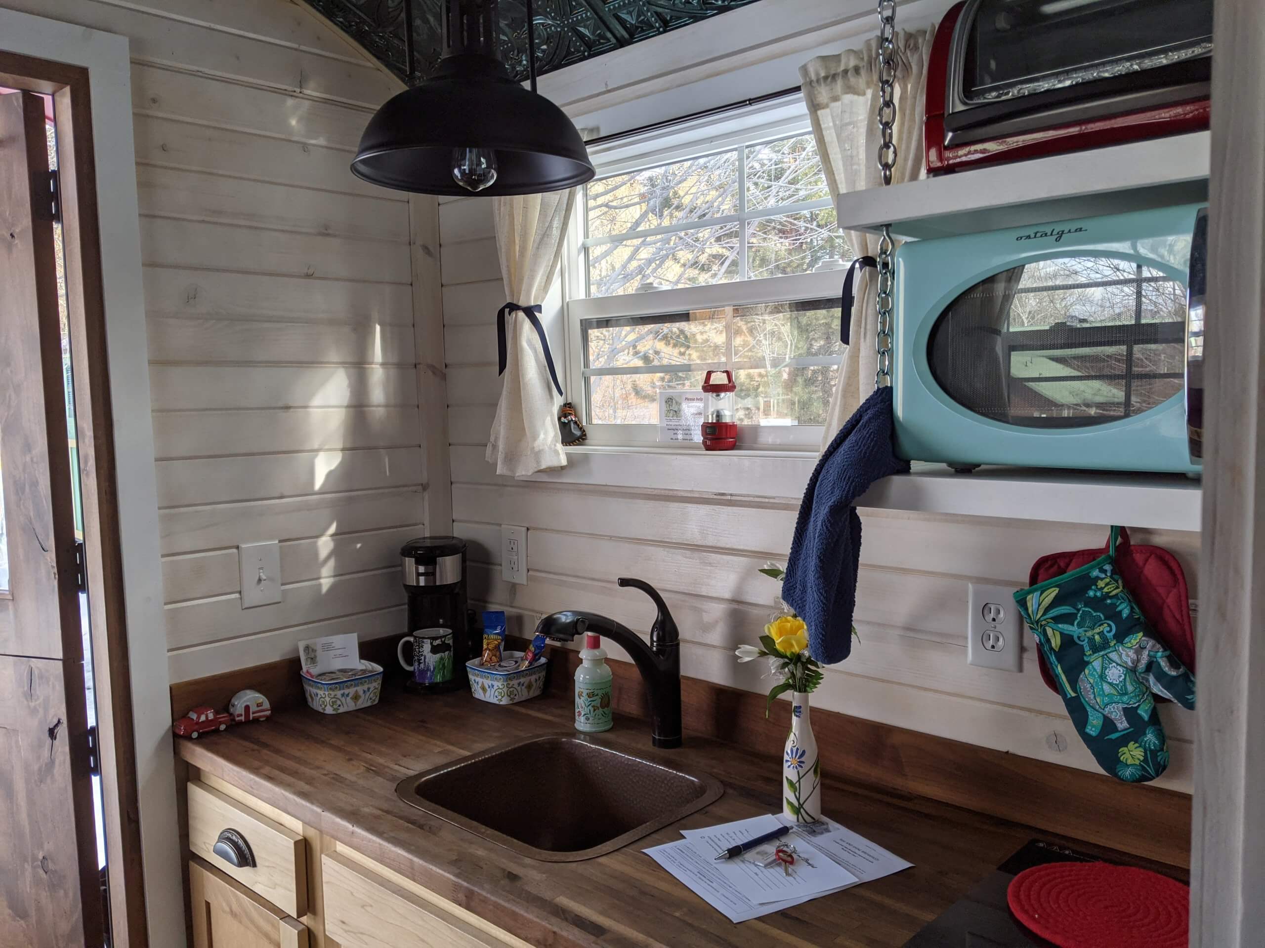 A bright day shines through the window of a kitchenette that holds a vase of yellow flowers inside the Salmon Gypsy B&B Wagons.