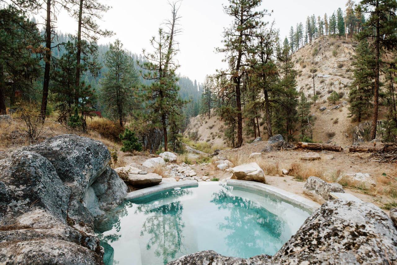 A stunning landscape view of the Southfork Springs Private Hot Springs surrounded by towering pine trees that reflect in the water.