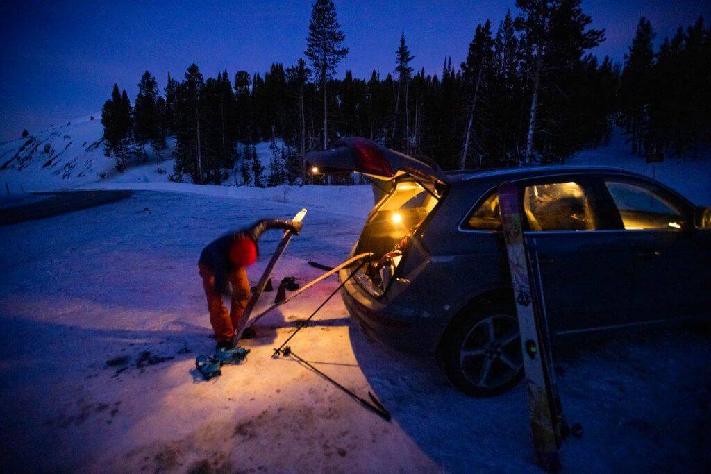 person putting skins on skis at dawn