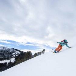 A woman in snow gear backcountry snowboarding down an alpine slope.