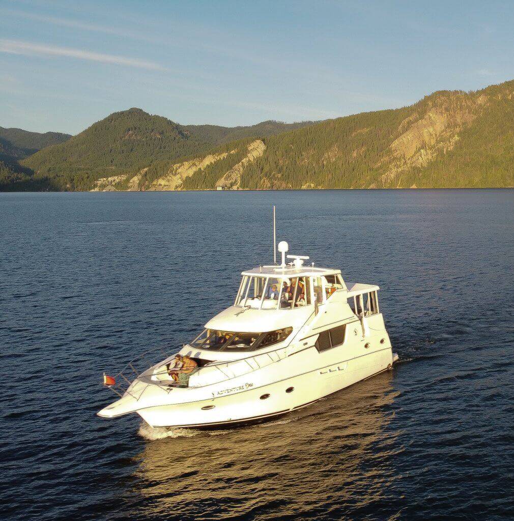 Picture of a white cabin cruiser boat on a dark blue lake with forested mountains and blue sky in the background.