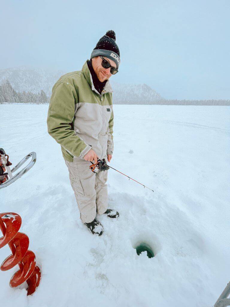 man standing on frozen lake while ice fishing