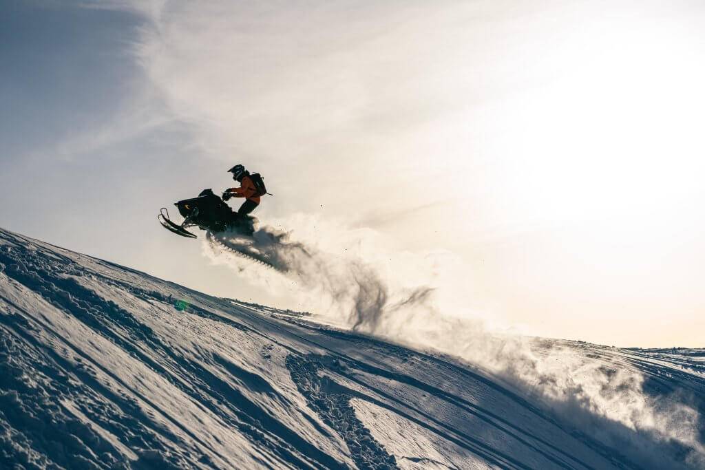 snowmobiler catching some area as its ascending the top of the hill