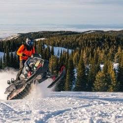 snowmobiler catching air at the summit of a snowy hill