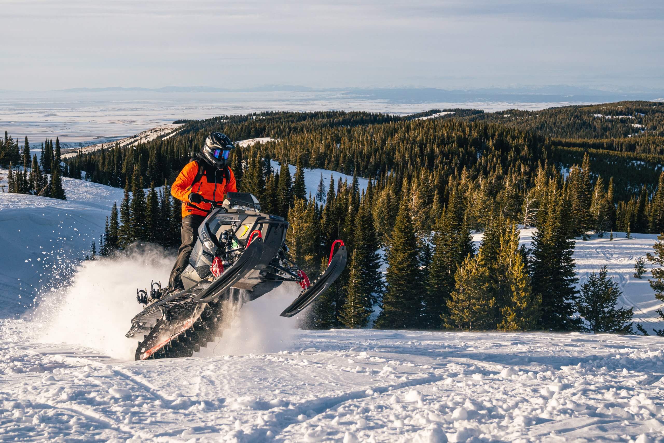 snowmobiler catching air at the summit of a snowy hill