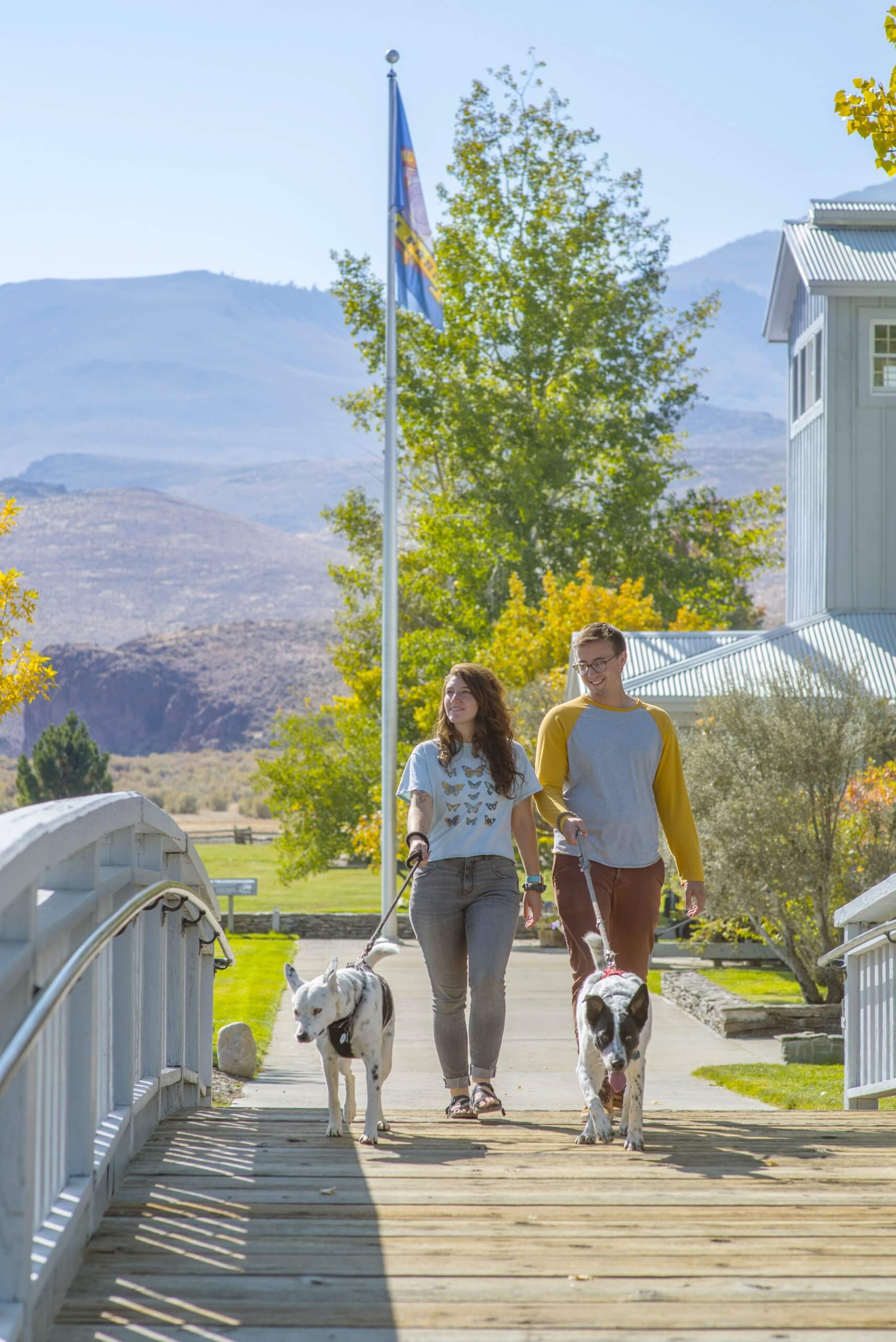 Two people walk two dogs across a footbridge at Land of the Yankee Fork State Park Visitor Center.