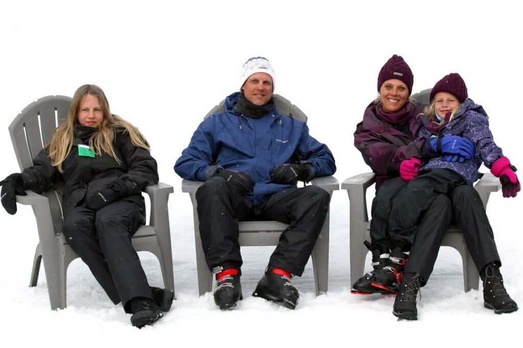 family sitting in chairs in snow gear with snow behind them