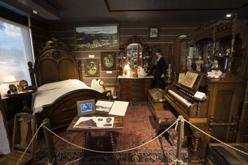 an exhibit of an old bedroom with antique, wooden furniture and a piano, at the Boundary County Historical Museum.