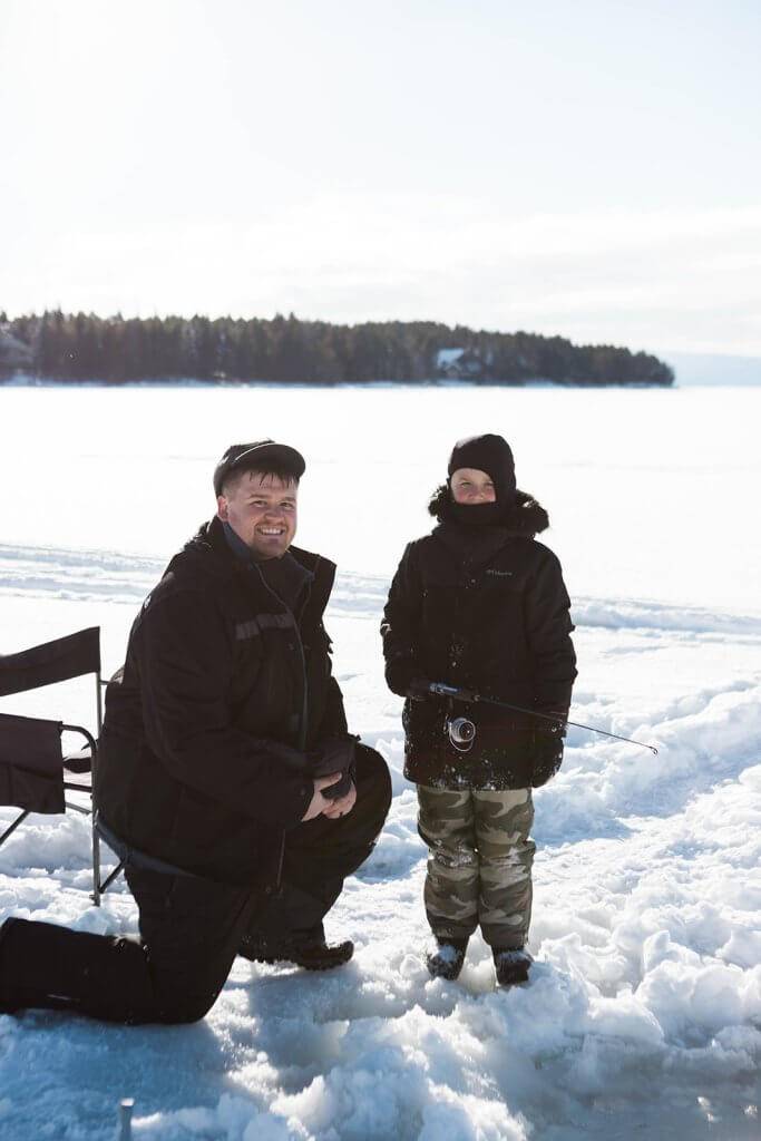 man and child standing at ice fishing hole with fishing poles