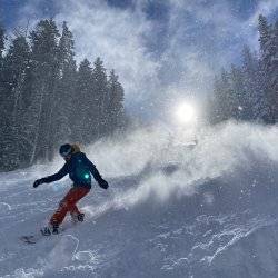 A snowboarder at Lookout Pass coming down a hill with the glowing sun in background.