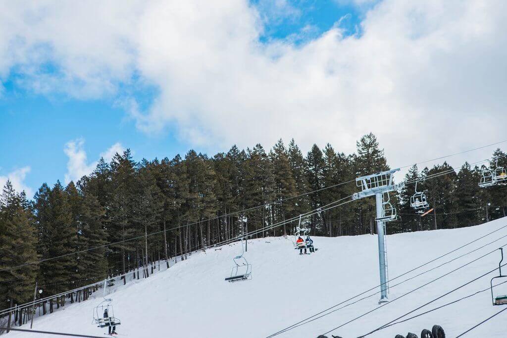 view of skiers on ski lift with trees in background