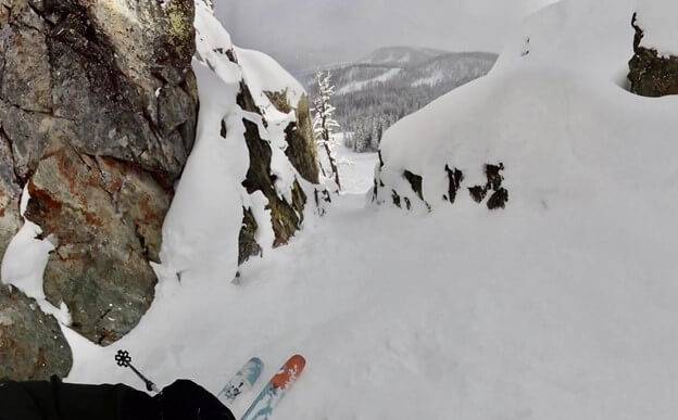 A skier showing the tips of their skis pointed down into a snow-filled couloir.