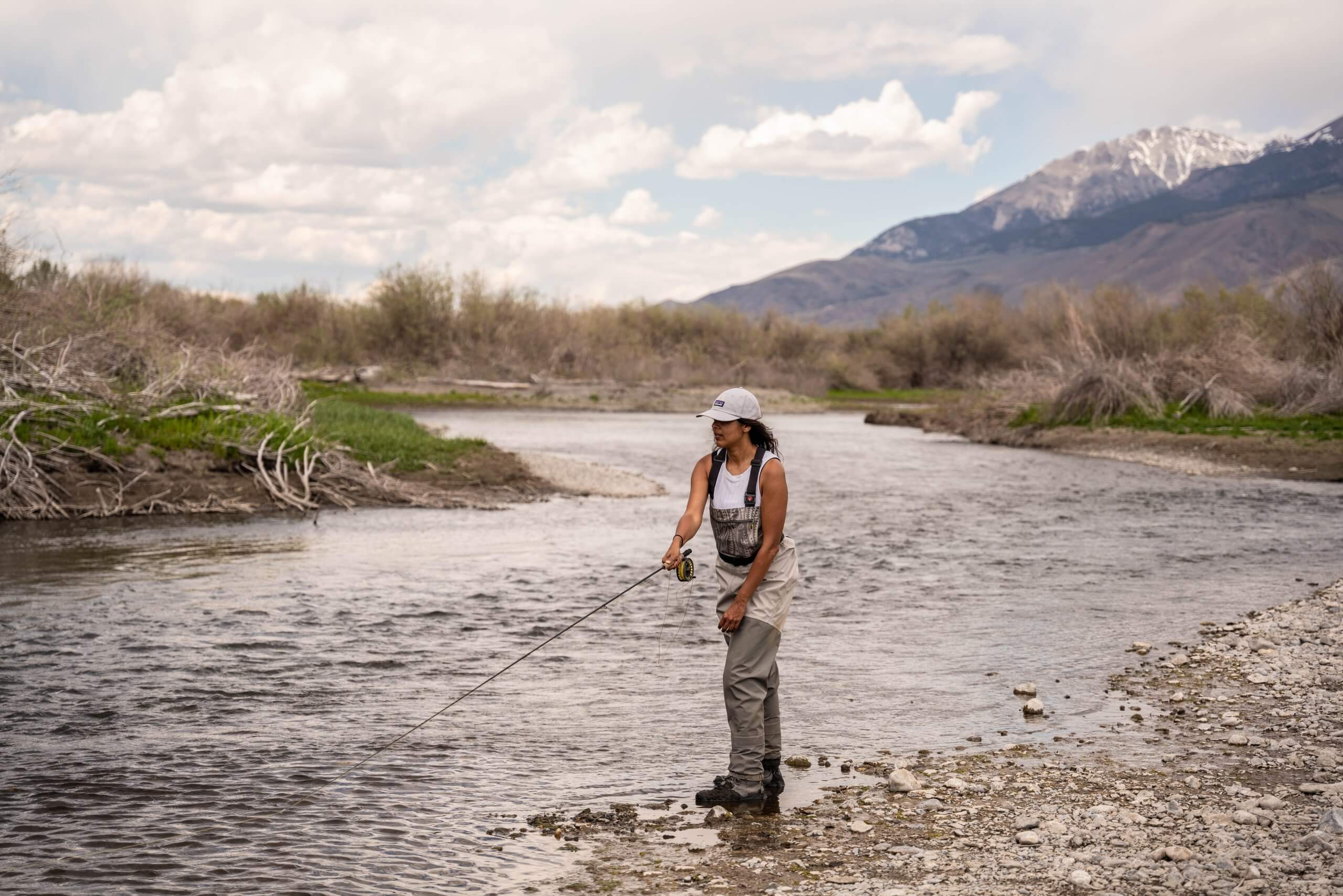 woman fly fishing in river with mountains in the background