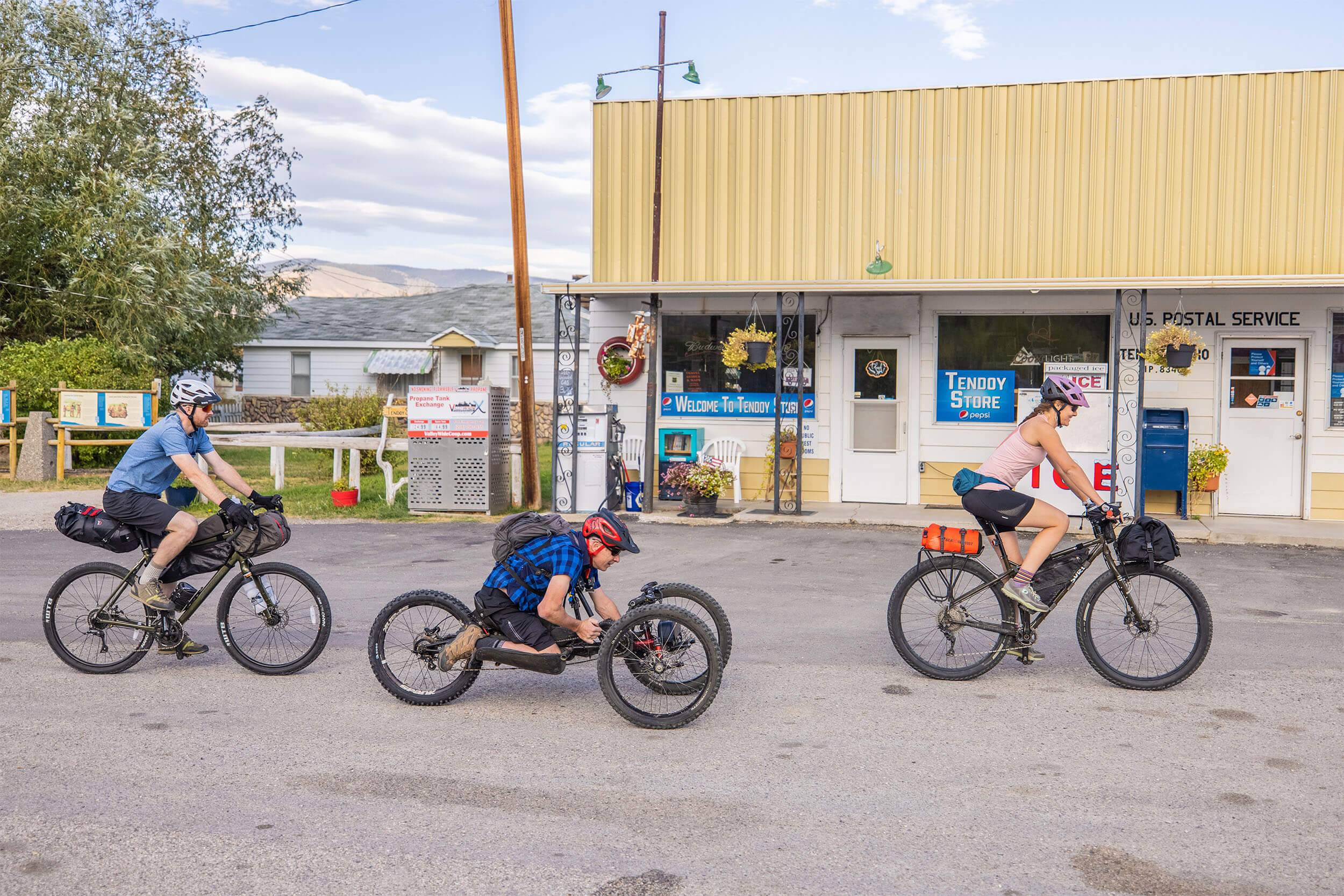 Bikers cycle along the road past the Tendoy Store