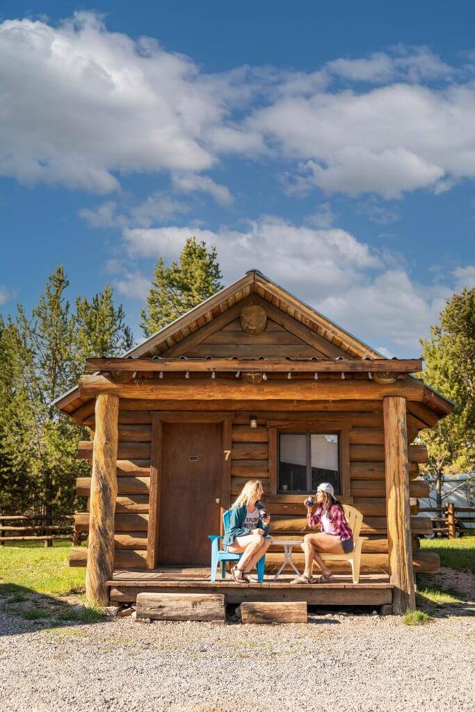 two women sitting on porch of small wooden cabin