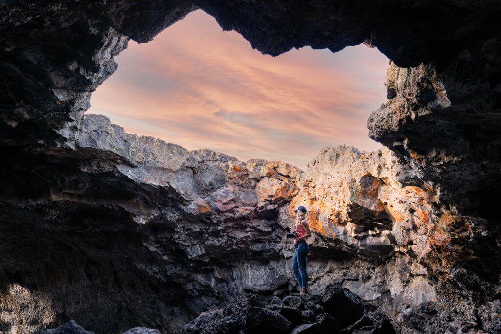 woman standing in rocky cave looking up at natural skylight