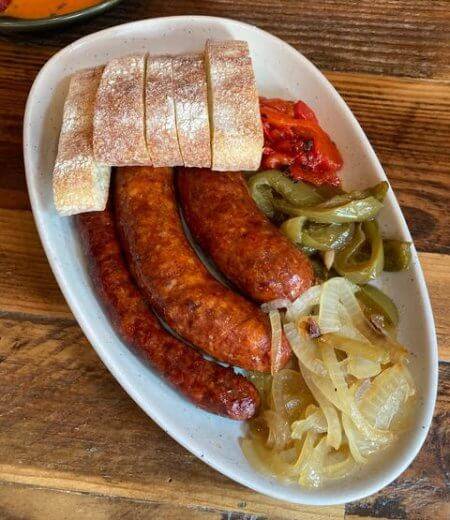 An overhead shot of chorizo sausages on an oval plate with bread and vegetables.