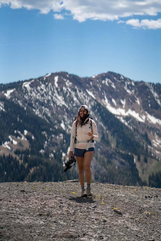 woman on hiking trail holding camera with mountains in background