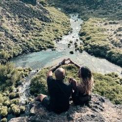 two people sitting on edge of rock overlooking pool of turquoise water with small river