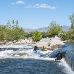 Surfboarders riding a wave and trees in the background at Boise Whitewater Park.