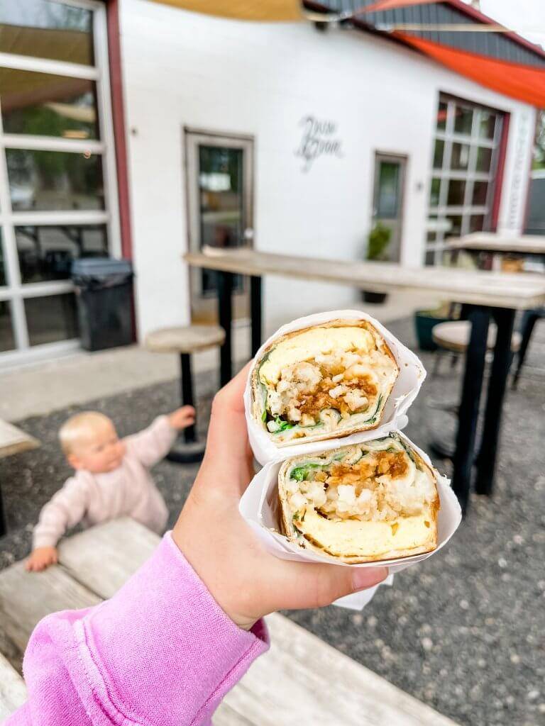 close up shot of breakfast burrito cut in half with building and child in background