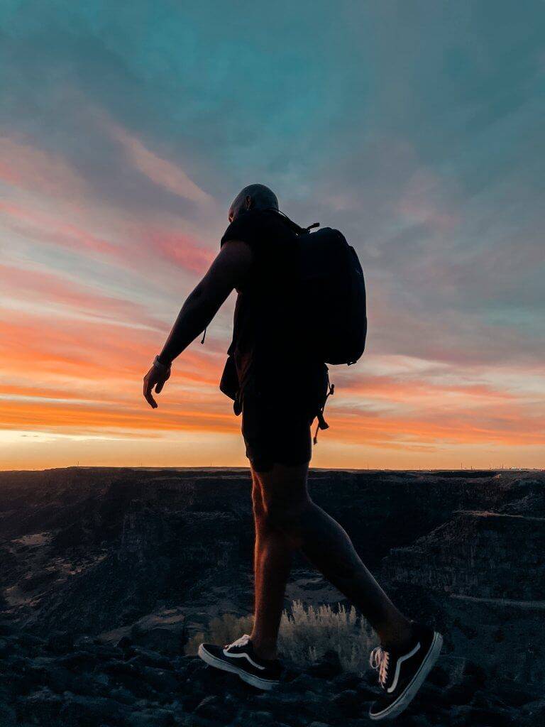 man standing on edge of rock canyon with sunset in the background