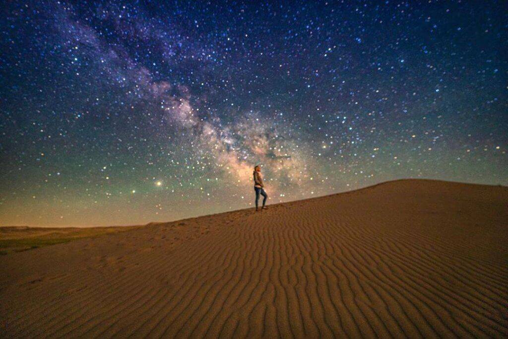 woman standing on sand dune with milky way overhead