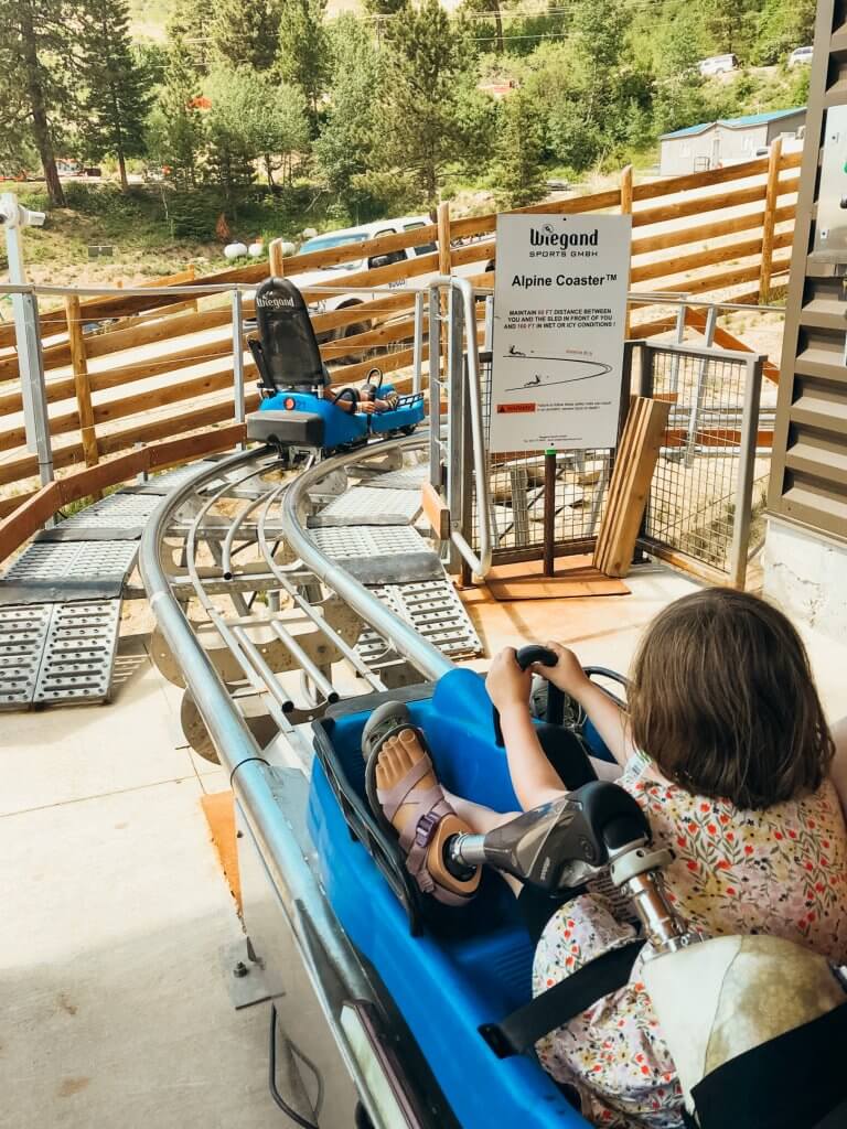 a girl sitting in the front of a roller coaster seat, her parent is behind her, but only her prosthetic leg is showing next to the daughter