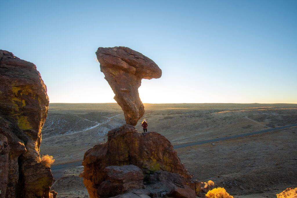 large oblong like rock standing perpendicular on another rock with a person standing next to it