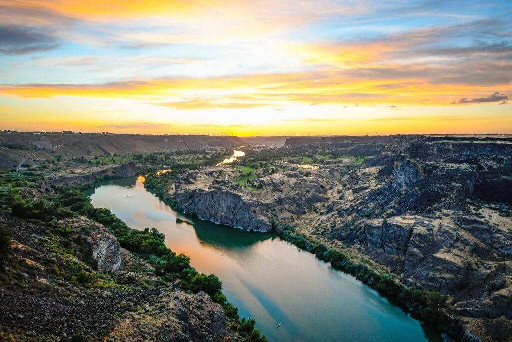 orange and yellow sunset over a deep canyon with the sunset reflecting off the water in the canyon