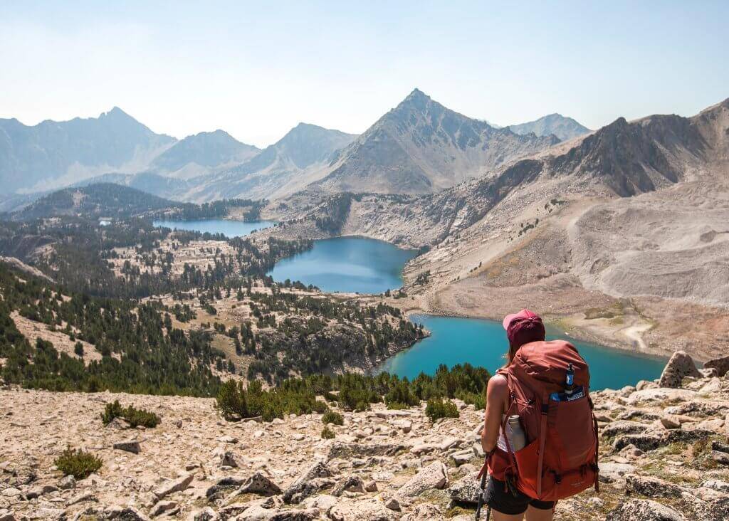 female backpacker standing on rocky hillside looking down at three alpine lakes in the distance